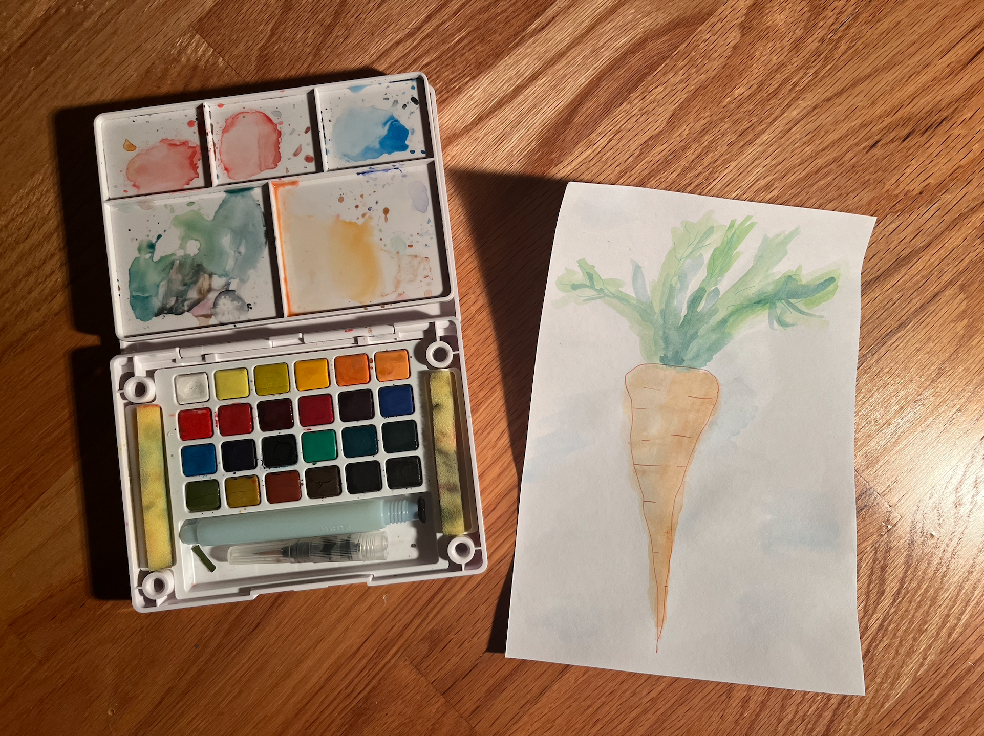 watercolor paints next to painting of carrot